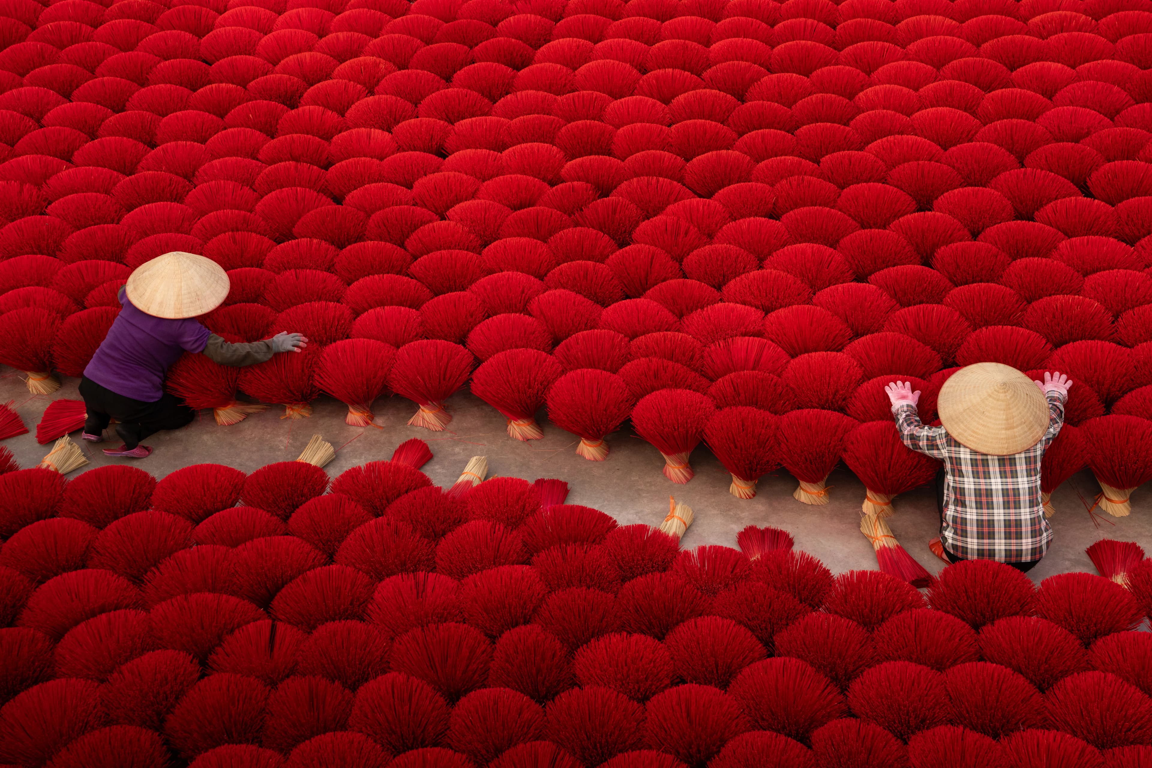 Two people arranging bright red incense bundles.