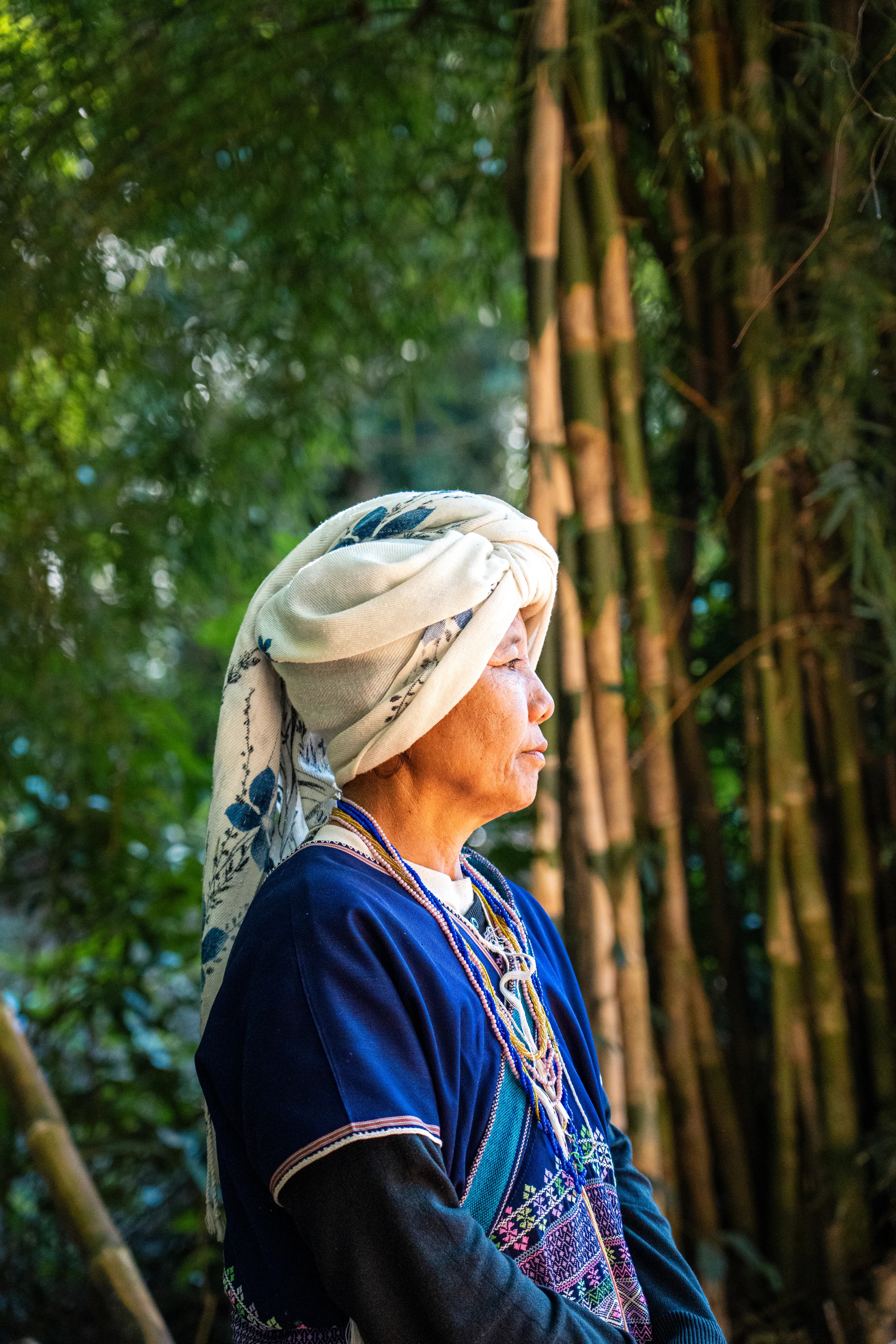 A woman in a patterned headscarf standing beside bamboo.